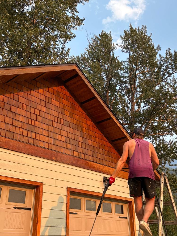 Nigel on a ladder spraying stain on a cedar shake gable above garage doors